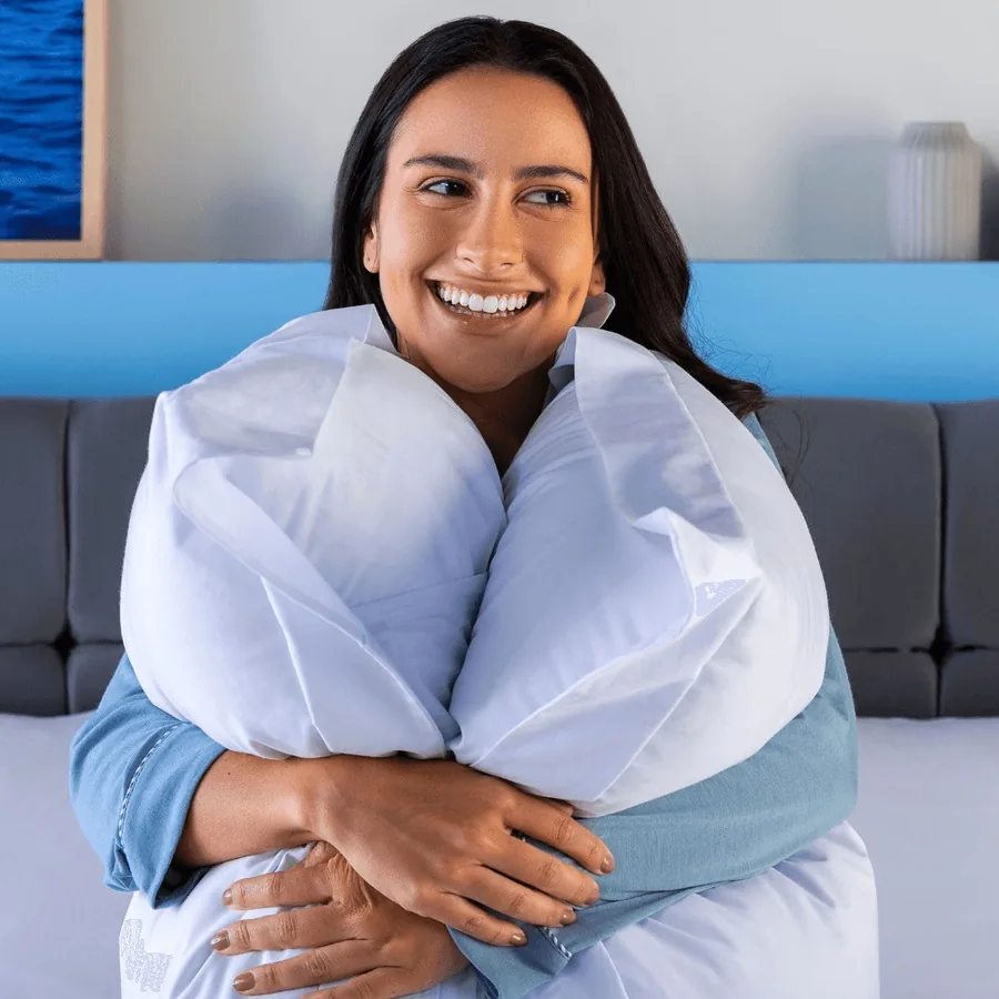 Mulher sorrindo abraçada a um travesseiro em casa